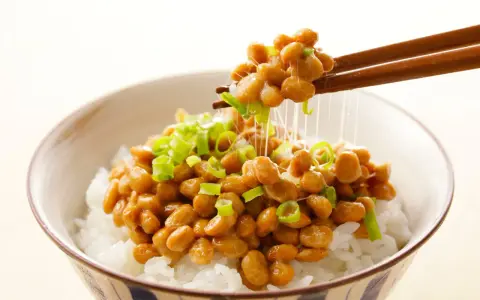 Miseczka ryżu z natto, japońską potrawą z fermentowanej soi, posypana szczypiorkiem. Pałeczki unoszą nitki natto.