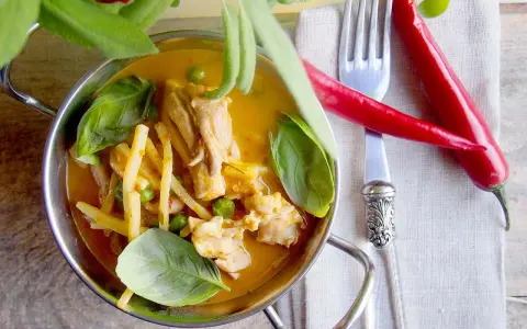 Aromatyczne czerwone curry z kurczakiem, bambusem i groszkiem, ozdobione świeżą bazylią i papryczkami chili.