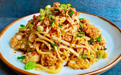 Pyszny makaron z wieprzowiną, posypany szczypiorkiem i sezamem, z dodatkiem płatków chili.