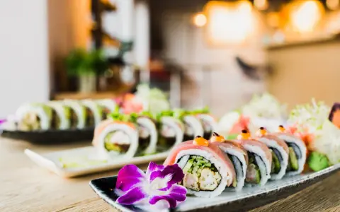 Wykwintne sushi z mięsem, ozdobione kwiatem i warzywami, prezentuje się apetycznie na talerzu.