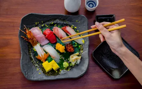 Wykwintne jedzenie w Japonii: ręka z pałeczkami sięga po świeże sushi i sashimi, obok sos i sake.