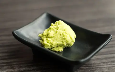 Zielona pasta wasabi na czarnej, kwadratowej miseczce. Zastanawiasz się wasabi co to? To ostry japoński chrzan.