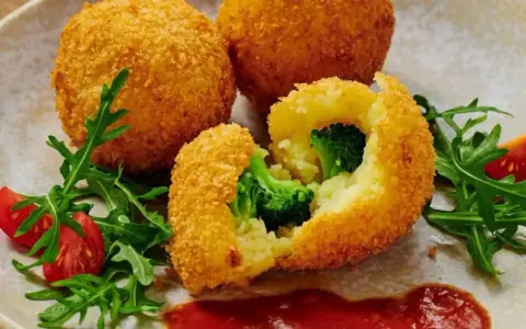 Chrupiące kulki ziemniaczane w panko z brokułami w środku, podane z rukolą i pomidorkami.
