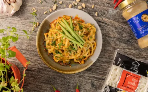 Udon co to? Makaron udon w kremowym sosie z orzeszkami ziemnymi i ogórkiem, obok paczka makaronu i tahini.