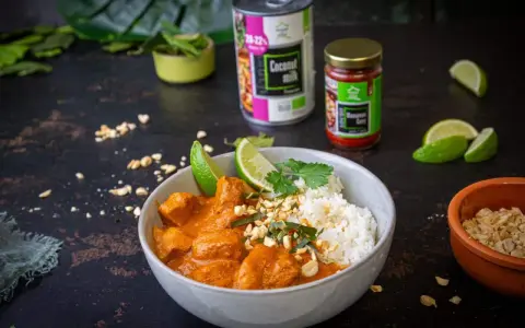 Aksamitny kurczak w sosie massaman curry, podany z ryżem, limonką i posypany orzeszkami. Obok puszka mleka kokosowego i słoiczek pasty massaman.