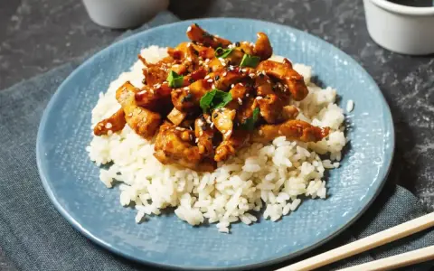 Pyszny kurczak po japońsku w sosie teriyaki, podany na ryżu z sezamem i szczypiorkiem. Idealny posiłek dla miłośników azjatyckich smaków.