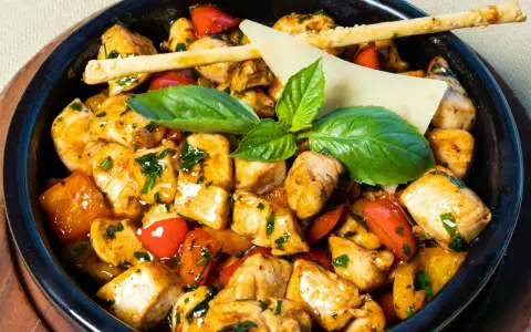 Kawałki kurczaka w sosie z papryką i ziołami, ozdobione listkami bazylii i paluszkami grissini. Danie przypomina egzotyczne jungle curry.