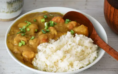 Pyszne japońskie curry z kurczakiem i warzywami, podane z ryżem i posypane szczypiorkiem.