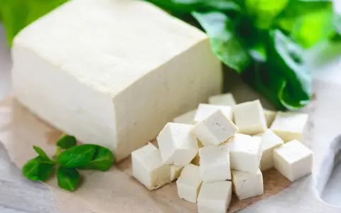 Kostka i pokrojone w kostkę tofu, obok zielone listki. Tak wygląda tofu – białe, delikatne, gotowe do przygotowania.