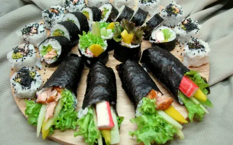 Talerz sushi z futomaki i uramaki. Widać rolki z łososiem, awokado, sałatą, paluszkami krabowymi i mango.
