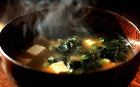 Gorący, parujący sos z pasty miso w drewnianej misce, z kostkami tofu i wodorostami.