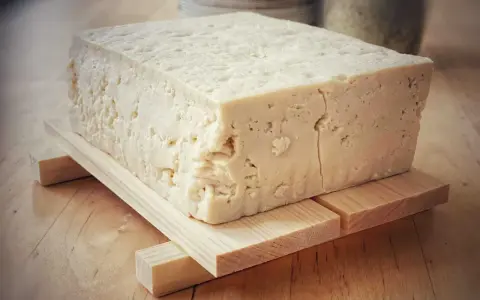 Duży blok domowego tofu na drewnianej podstawce, gotowy do przygotowania pysznych dań.