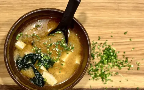 Miseczka aromatycznego miso shiru z tofu i wodorostami, posypana szczypiorkiem.