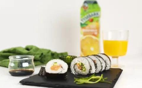 Pyszne sushi z łososiem, ogórkiem i ryżem, podane z sosem sojowym i sokiem pomarańczowym.