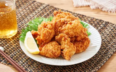 Chrupiące karaage chicken na talerzu, ozdobione plasterkiem cytryny i liśćmi sałaty. Obok szklanka złocistego napoju i pałeczki.