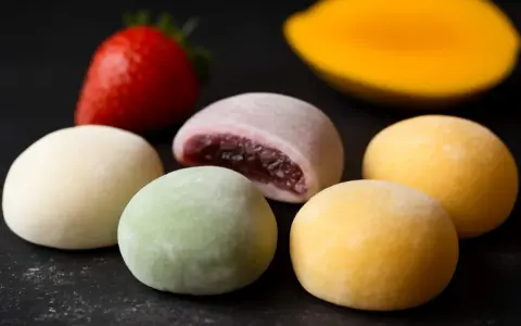 Kolorowe mochi, jak jeść? Delikatne kuleczki z nadzieniem, obok truskawka i mango.