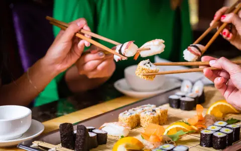 Ręce trzymają pałeczki, jedząc sushi. To smakowita uczta, która odzwierciedla japońskie tradycje kulinarne.