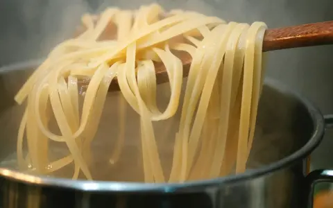 Gorący makaron mie unoszony na drewnianej łyżce nad parującym garnkiem. Idealny przepis na szybki obiad.