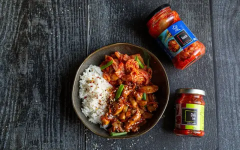 Miseczka ryżu z kurczakiem w sosie i kimchi, obok słoiczki z kimchi i pastą chili.