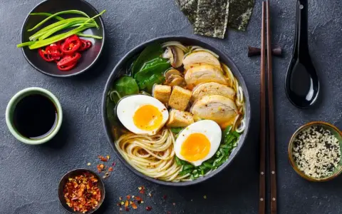 A miseczce aromatycznego ramenu z tofu, jajkiem na pół, kurczakiem i zieloną cebulką. Obok sos sojowy, chili i nori.