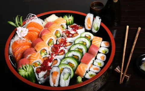 Talerz pełen różnorodnych sushi, w tym nigiri z łososiem i tuńczykiem, rolki z ogórkiem i awokado, a także kilka kawałków temaki sushi.