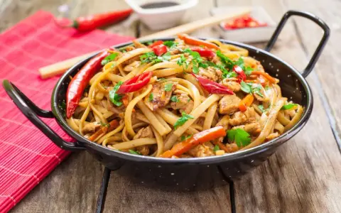 Pyszny makaron chain main z kurczakiem, papryką i chili, posypany natką pietruszki, w czarnej woku.