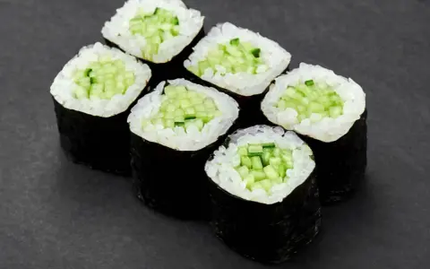 Sześć kawałków sushi z ogórkiem, ułożonych na ciemnym tle.