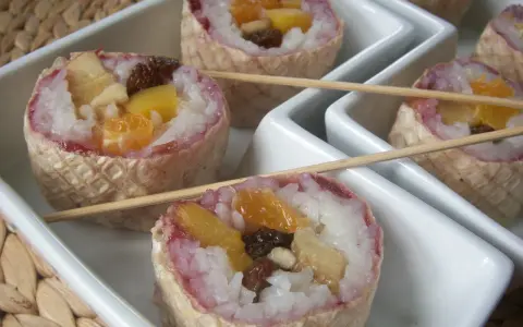 Słodkie sushi owocowe w wafelkach, z ryżem i kawałkami owoców, podane na białych tacach.