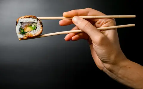 Dłoń trzyma pałeczkami jedno sushi. Zastanawiasz się, ile sushi na osobę będzie idealne na kolację?