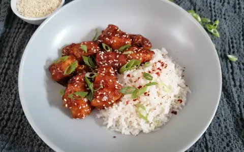 Pyszny kurczak po koreańsku w sosie, posypany sezamem i szczypiorkiem, podany z ryżem.