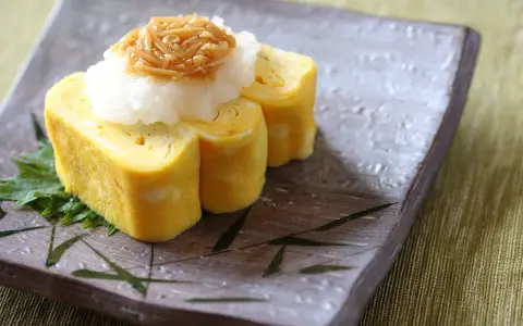 Roladki tamago z tartą rzodkwią i grzybami enoki na talerzu z motywem bambusa.