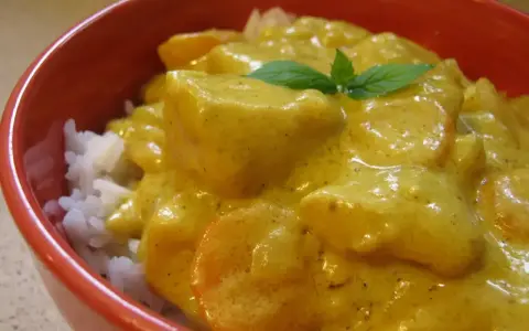 Miseczka ryżu z kurczakiem w kremowym sosie z curry, ozdobiona listkiem mięty.