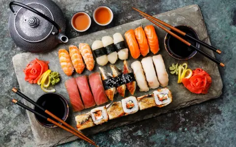 Piękne składniki na sushi: nigiri z łososiem, krewetkami, tuńczykiem, węgorzem i rybą maślaną, a także rolki. Obok czajniczek, sos sojowy i marynowany imbir.