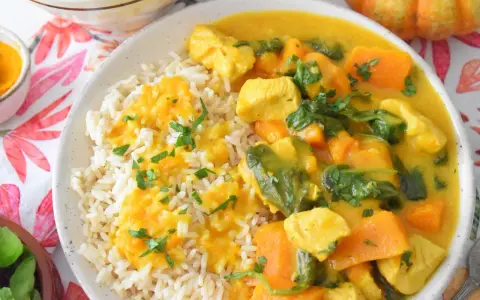 Aromatyczny kurczak curry z dynią i mlekiem kokosowym, podany z ryżem i posypany natką pietruszki.