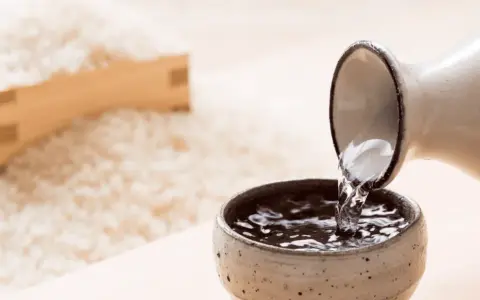 Sake przelewana z dzbanka do czarki, w tle ryż. Poznaj, jak smakuje sake.
