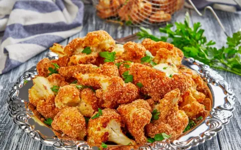 Chrupiący kalafior w panko, podany na ozdobnej tacy, posypany świeżą natką pietruszki. Idealna przekąska!