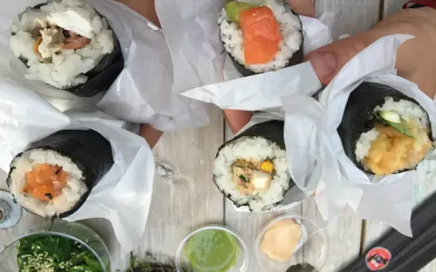 Ręcznie robione handroll sushi z łososiem, awokado, tuńczykiem i krewetkami. Pyszne przekąski na drewnianym stole.