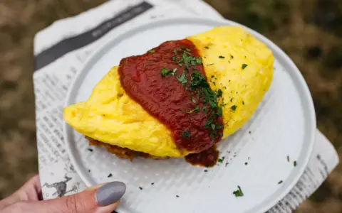 Pyszny omlet ryżowy polany sosem pomidorowym i posypany natką pietruszki, podany na talerzu.