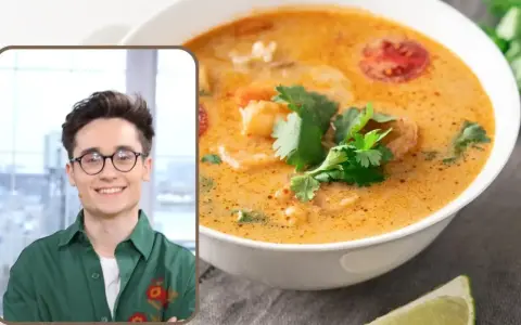 Uśmiechnięty mężczyzna w okularach prezentuje aromatyczną zupę tajską z krewetkami i pomidorkami, ozdobioną świeżą kolendrą.