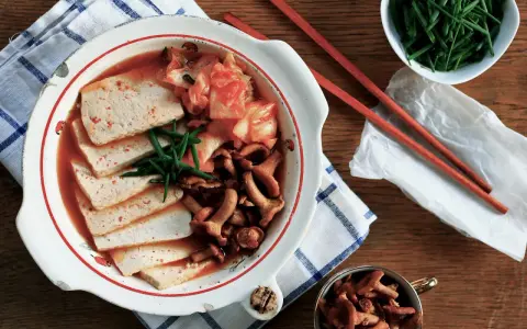 Pyszne kimchi jjigae z tofu i grzybami, podane z zieloną cebulką.