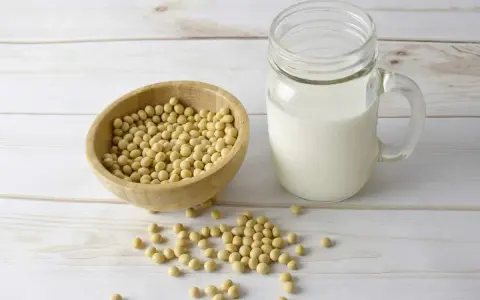 Misternie ułożone ziarna soi w drewnianej misce i szklanka mleka sojowego. Czy soja ma gluten? Nie, soja jest bezglutenowa.