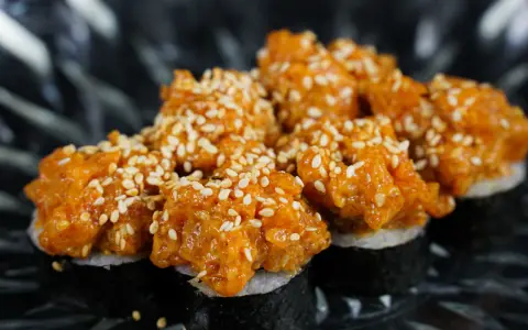 Pyszne sushi z tatarem z łososia, posypane sezamem, prezentuje się apetycznie na ciemnym talerzu.
