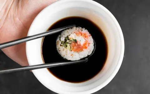 Pałeczkami zanurzam rolkę sushi w ciemnym sosie. Idealny sos słodki do sushi podkreśla smak ryby i ryżu.