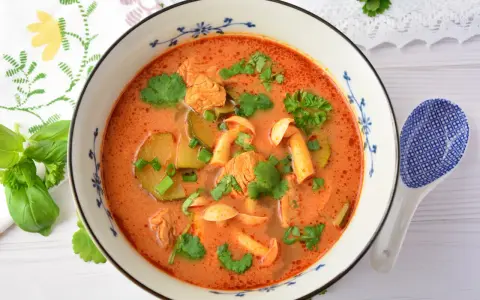 Aksamitny tom yum z kurczakiem, grzybami i kolendrą w misce z niebieskim wzorem. Obok leży łyżka.