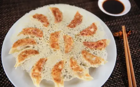 Chrupiące pierożki gyoza ułożone na talerzu, z chrupiącą panierką z ciasta. Obok miseczka sosu sojowego i pałeczki.
