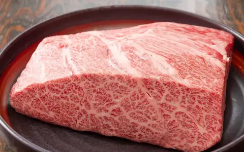Wyjątkowy kawałek wołowiny wagyu z widocznym marmurkowym przerostem tłuszczu, prezentowany na ciemnej tacy.