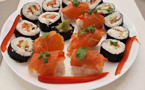 Piękne sushi kompozycje na białym talerzu: rolki z łososiem, awokado i papryką, ozdobione kolendrą.