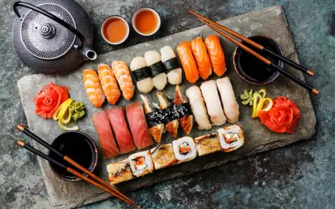Zestaw sushi: nigiri z łososiem, krewetkami, tuńczykiem, węgorzem i rolki. Obok czajniczek, miseczki z herbatą i sos sojowy. Tak jedzą japończycy.