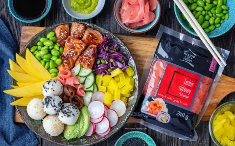 Kolorowy bowl z kawałkami glazurowanego lososia, ryżem, awokado, mango, ogórkiem, rzodkiewką, edamame i marynowanym imbirem. Obok opakowanie różowego imbiru.