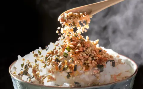 Łyżka sypie na parujący ryż kolorowy furikake. To japońska posypka, która dodaje smaku.